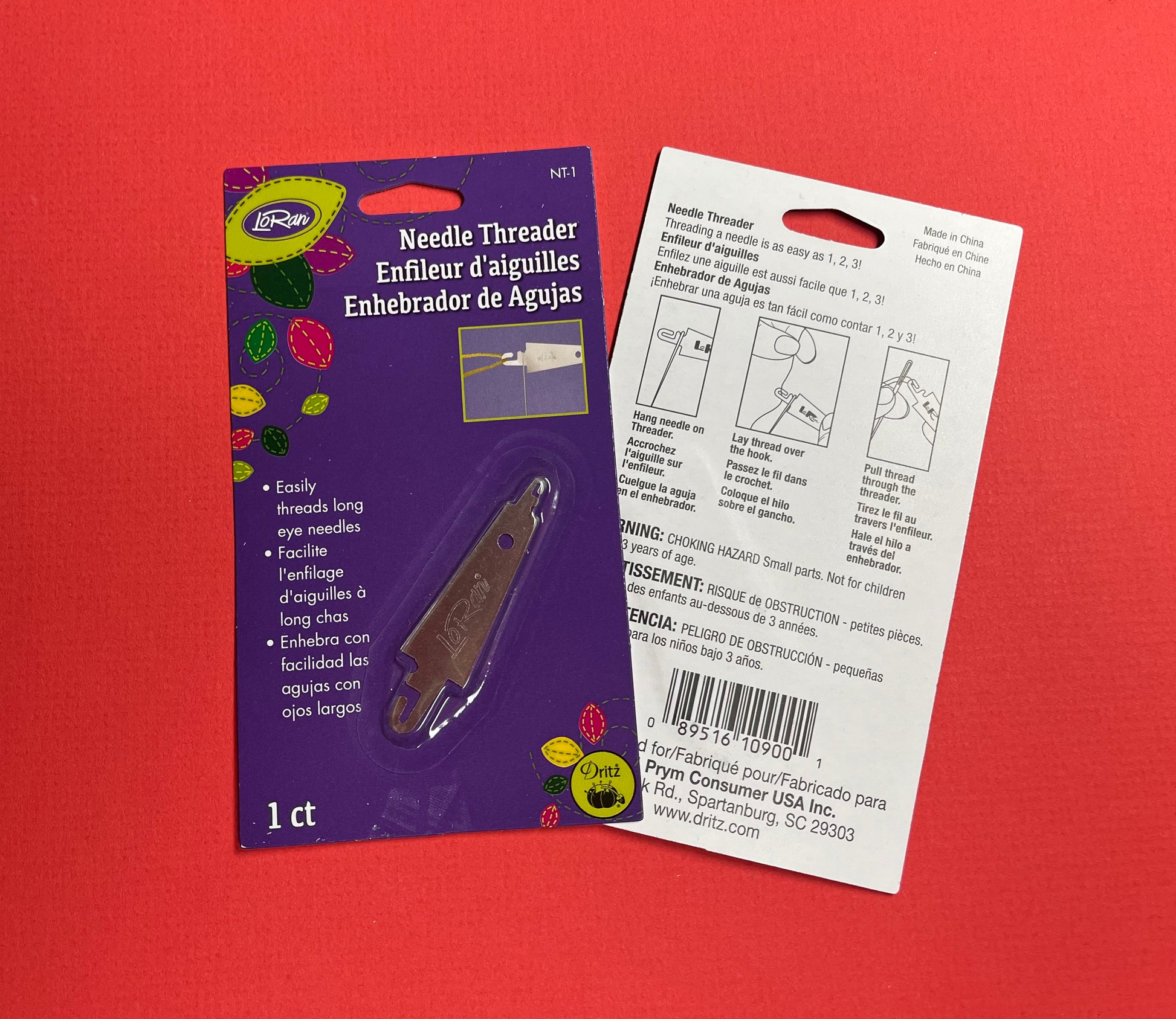A packaged needle threader for embroidery needles. There are two sizes, one on each end. It's shown on a red background, with the front retail card and the back instruction card visible. 